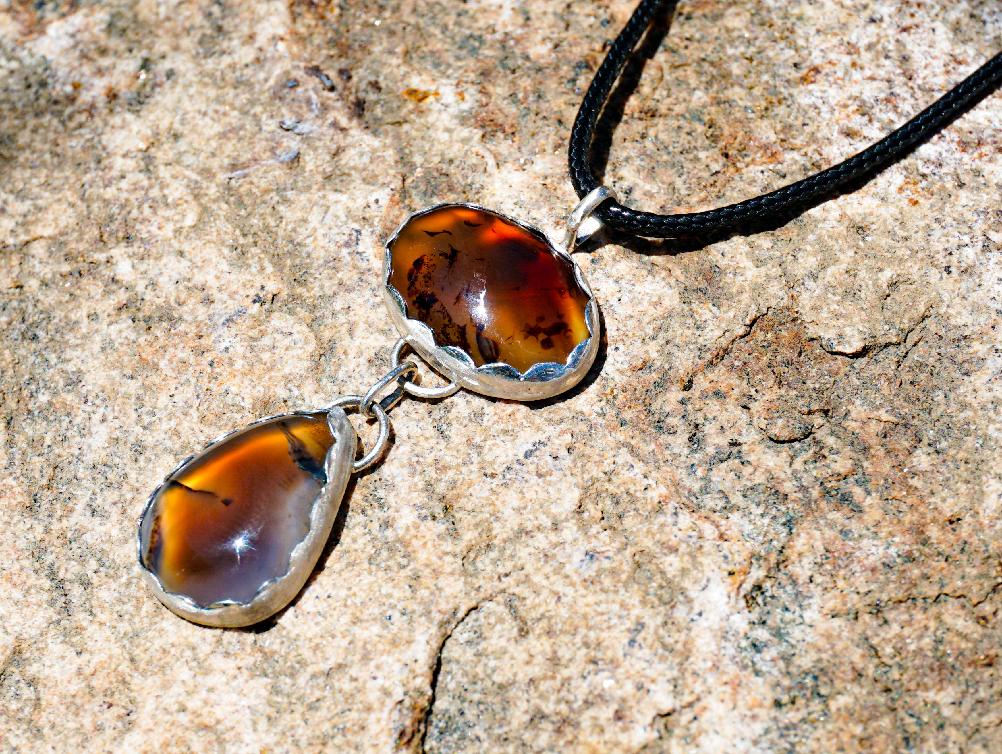 Sterling silver pendant with two linked Montana agate stones on a black nylon cord, displayed on natural stone background.