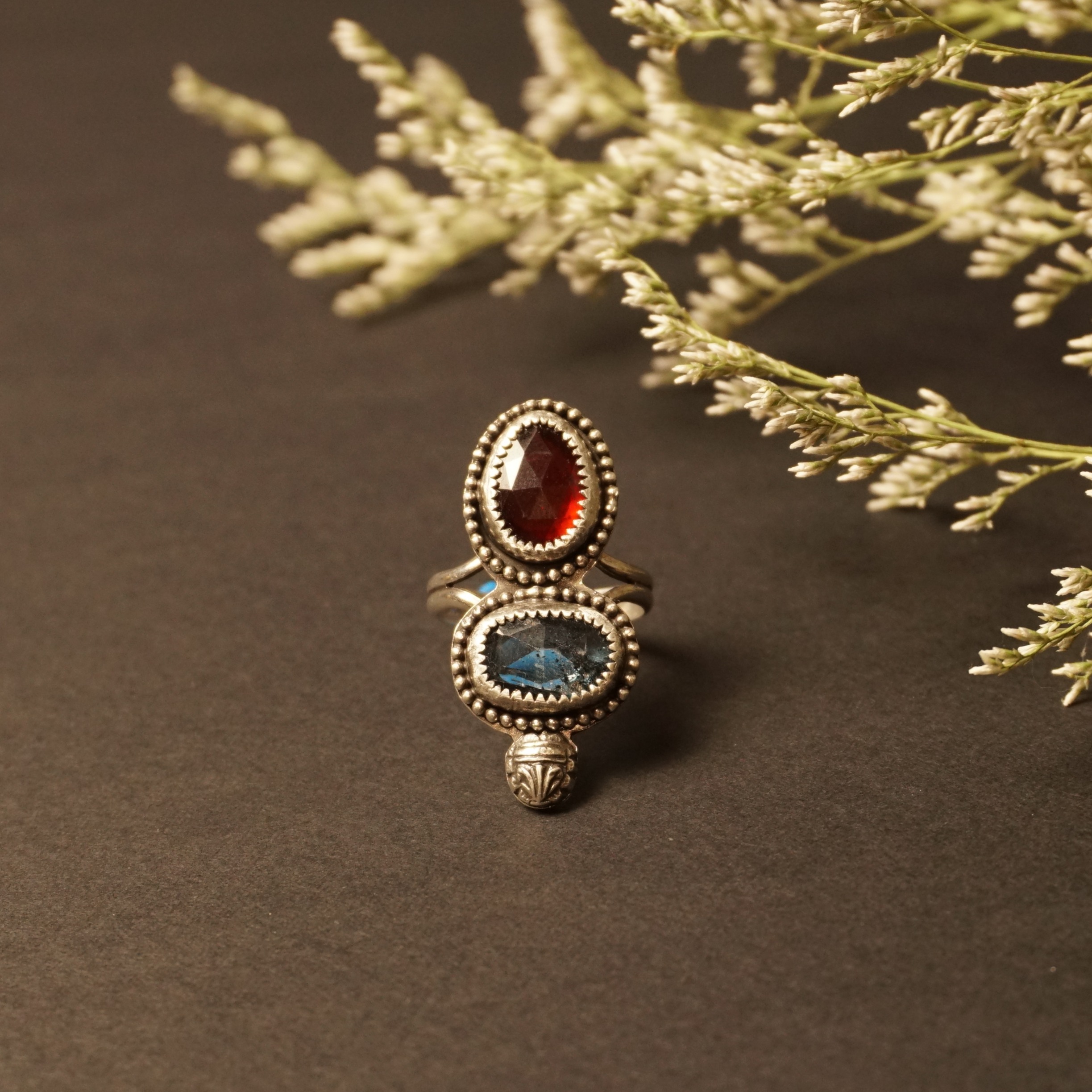 Handmade sterling silver ring with glowing hessonite garnet and teal moss kyanite stones in bezel settings, front view in soft natural light