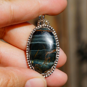 Step into the magic of the northern lights with this handcrafted sterling silver pendant featuring a mesmerizing multi tiger eye stone. The stone shimmers with deep greens, blues, and earthy gold tones, reminiscent of an aurora dancing across the night sky. The open-back design shows the beauty of the stone as it was too beautiful to be covered🤩, highlighting the stone's natural beauty and creating a captivating play of colors. Metaphysical Properties: The multi tiger eye is known for its grounding and protective energy. Often referred to as the “Stone of Balance,” it helps align the mind, body, and spirit, promoting mental clarity and emotional stability. This gemstone is believed to ward off negativity, encourage self-confidence, and provide a calming energy during times of stress. Wear it to feel centered, focused, and connected to nature’s beauty. This pendant is ideal as a unique gift or a meaningful addition to your own jewelry collection. Whether worn casually or dressed up, it’s sure to draw attention, compliments, and a little extra positivity in your day!!