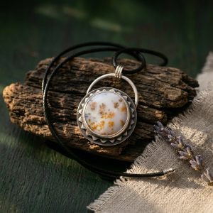 Scenic dendritic opal pendant propped facing left on beachwood with fresh lavender, showing autumn leaf inclusions in sterling silver sun setting