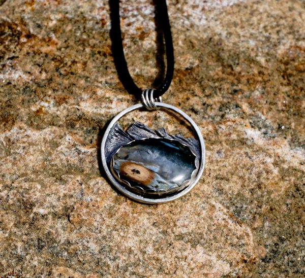 Ocean jasper pendant on natural stone surface with mountain carving details.