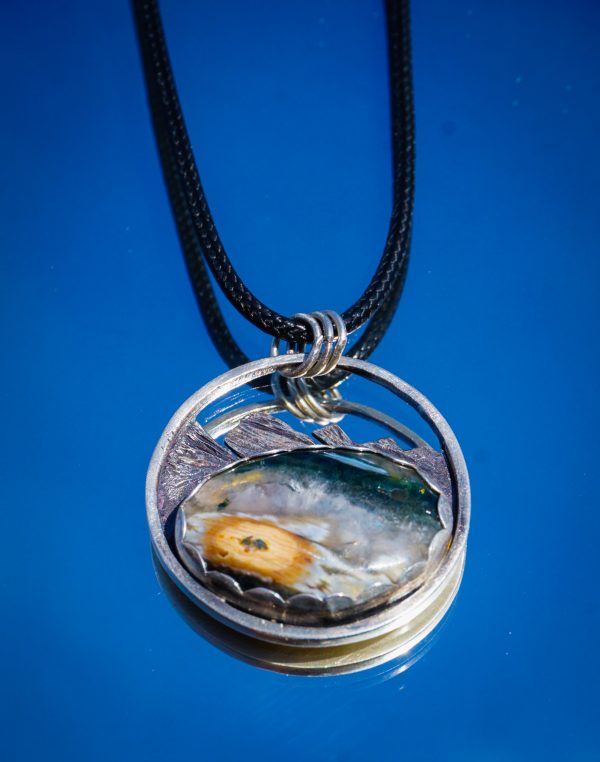 Sterling silver ocean jasper pendant with mountain carving, set against blue sky.